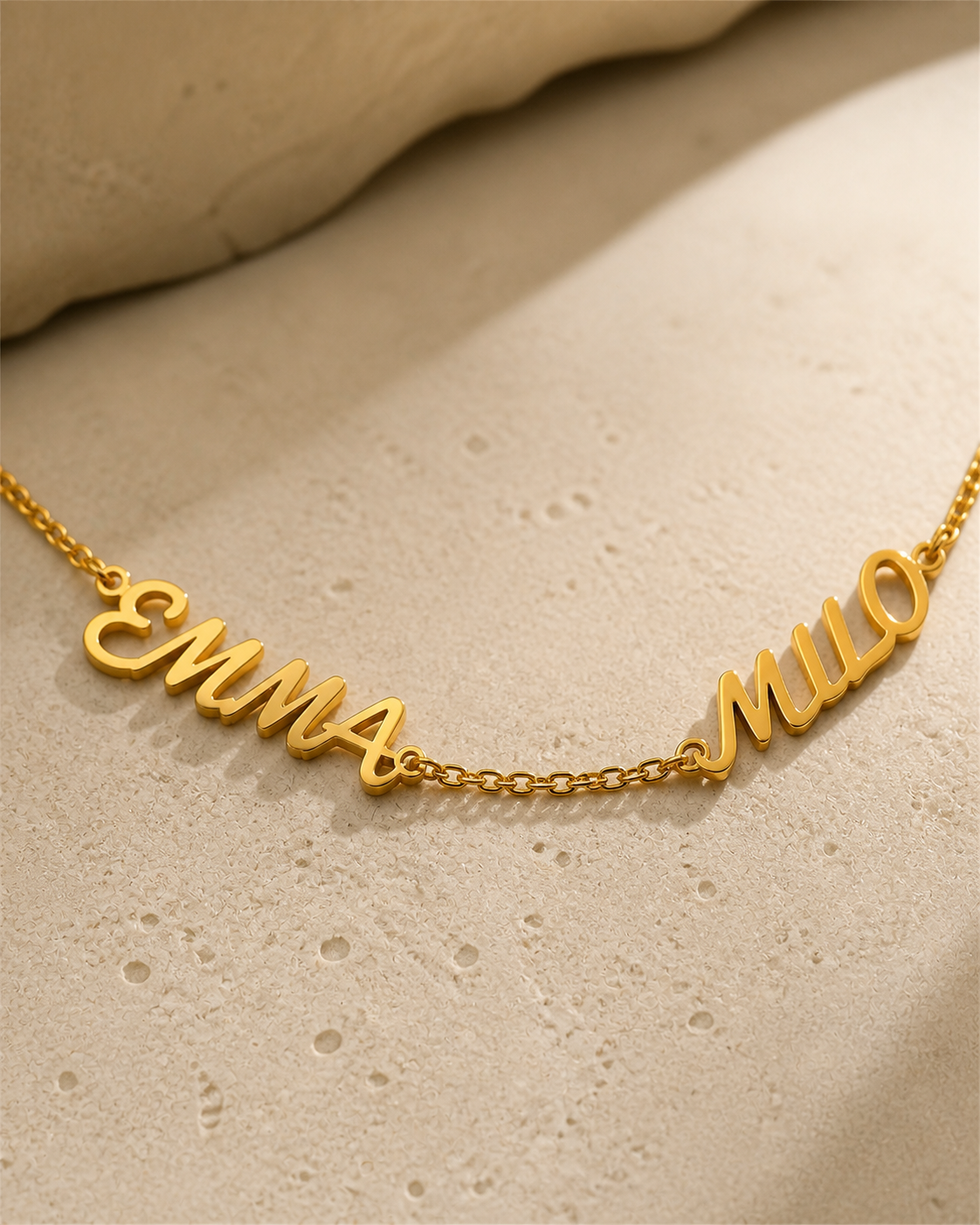 Names Between Us Necklace in 18K yellow gold finish on a textured mineral surface